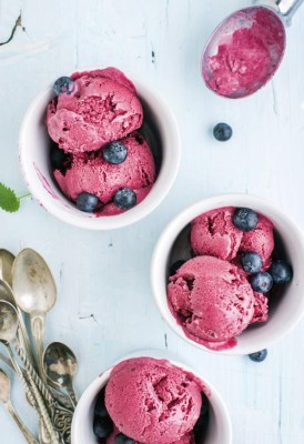 Homemade blueberry ice cream scoops with fresh berries and mint leaves in cups over light blue background, Top view, selective focus