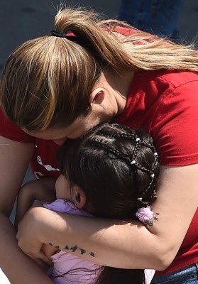 A woman hugs a girl after she and other North Park Elementary School students were released to their guardians following a shooting at the school which left two adults and one child dead, April 10, 2017 at Cajon High School in San Bernardino California. A gunman opened fire at an elementary school in the California city of San Bernardino, killing one woman and wounding two students before turning the gun on himself, police said. The students were airlifted to a local hospital where their conditions were described as critical. / AFP PHOTO / Robyn Beck