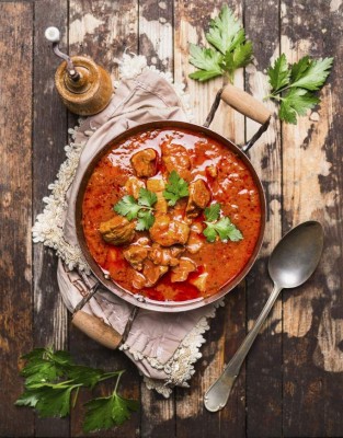 beef stew or goulash in old pan served with spoon and napkin on rustic wooden background, top view