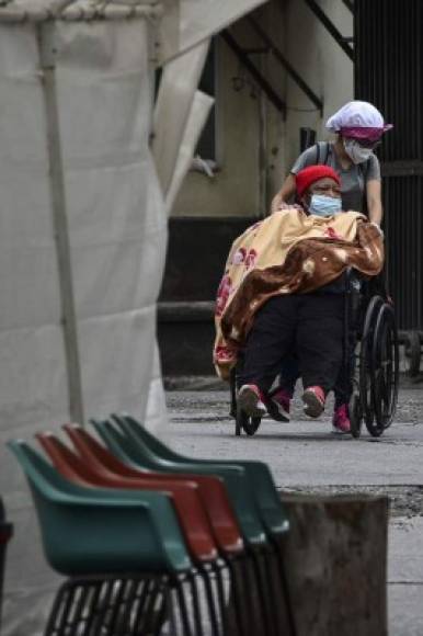 Un paciente infectado con COVID-19 es empujado en una silla de ruedas por una mujer en un hospital público. AFP