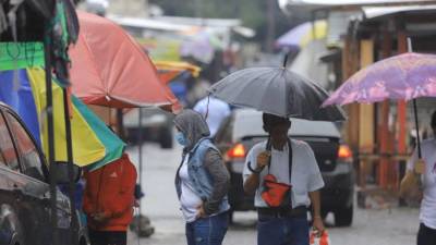 Hondureños caminan por el centro de San Pedro Sula mientras llueve.