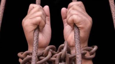 Manos de mujer tomando los barrtotes de una celda | Fotografía de archivo