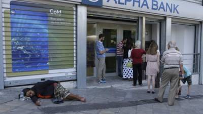 Un mendigo duerme en la acera mientras varias personas hacen fila frente a un banco en Atenas.