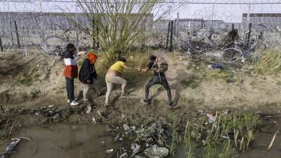 Un grupo de migrantes intenta cruzar una alambrada tras atravesar el río Bravo en el sur de Texas.