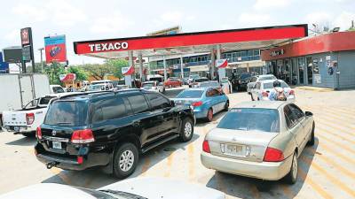 Vehículos hacen fila para cargar combustible en una gasolinera.
