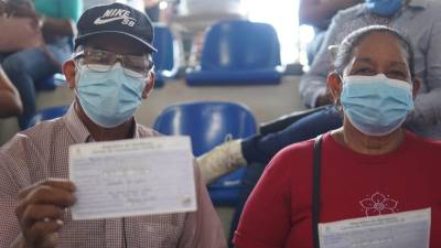 Hondureños muestran el carné de vacunación contra el coronavirus.