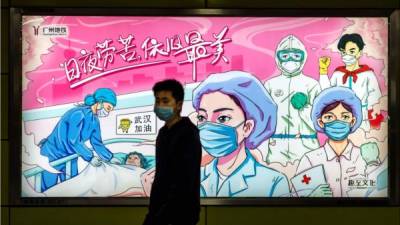 Un hombre con una máscara protectora camina frente al cartel de propaganda de lucha contra el coronavirus en Guangzhou, provincia de Guangdong, China. Foto EFE