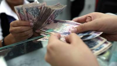 Un cliente recibe dinero en moneda nacional de parte de un agente bancario.