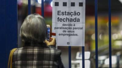 Una mujer toma una foto frente al portón cerrado de una estación del metro en Sao Paulo