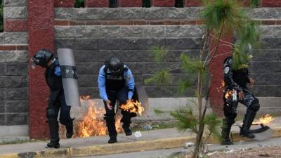 Riot police officers and a member of the Cobra Special Unit trying to disperse students of the National Autonomous University of Honduras (UNAH) gathered under the University Student Movement (MEU) who were blocking a boulevard to demand, among other things, the resignation of rector Julieta Castellanos, are hit with a Molotov cocktail during clashes in Tegucigalpa, on July 25, 2017.The MEU, who is occupying several buildings of the UNAH since June 13 preventing some 50,000 students from attending classes, also demands the cessation of the 'criminalization' of protests, the suspension of student hearings and support to appoint delegates to the University Council, UNAH's main decision-making body. / AFP PHOTO / Orlando SIERRA