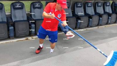 Marvin Martínez, utilero del Olimpia, limpiando con una escoba las cosas que deja Diego Vázquez en el banquillo visitante.