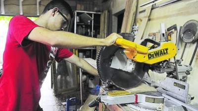 Un joven manipula un cortador de madera.