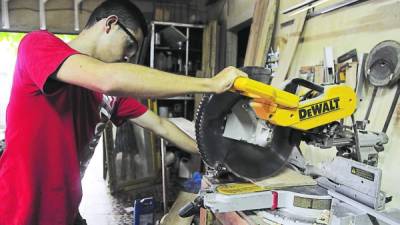 Un joven manipula un cortador de madera.