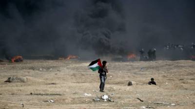 TOPSHOT - A man holds a Palestinian flag during clashes with Israeli forces near the border between the Gaza strip and Israel, east of Gaza City on May 14, 2018, following the the controversial move to Jerusalem of the United States embassy. Fifty-two Palestinians were killed by Israeli fire during violent clashes on the Gaza-Israel border coinciding with the opening of the US embassy in Jerusalem, the health ministry in the strip announced. / AFP PHOTO / THOMAS COEX