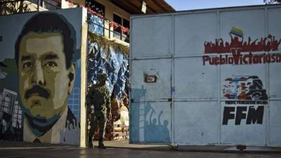 Soldados venezolanos caminan junto a al mural de una escuela en el que aparece la imagen de Nicolás Maduro en Caracas.