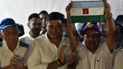 El candidato opositor a gobernador del Estado Barinas, Sergio Garrido celebra sosteniendo una bandera junto al excandidato Freddy Superlano, durante una conferencia de prensa.