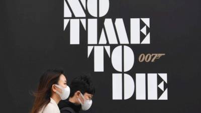Personas que llevan máscaras protectoras pasan un póster de la nueva película de James Bond.