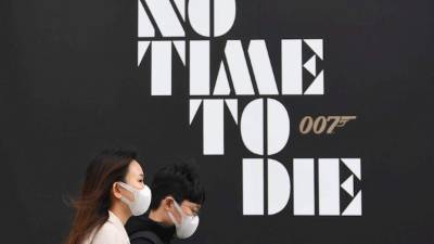 Personas que llevan máscaras protectoras pasan un póster de la nueva película de James Bond.