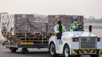 Los trabajadores del aeropuerto transportan en plataformas rodantes un envío de vacunas covid-19 del programa de vacunación global de Covax. Foto AFP