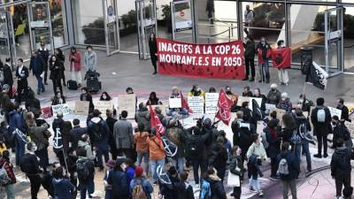 Los activistas de ‘Extinction Rebellion’ son observados por transeúntes mientras posan con una pancarta que se traduce como ‘Inactivo en la Cop 26 muriendo en 2050’.