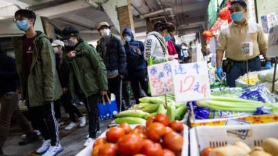 El propietario de un puesto de verduras (R) con una máscara facial en un mercado húmedo. Foto AFP