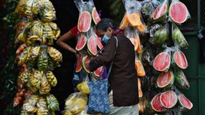 Una mujer usa una máscara facial como medida preventiva contra la propagación del coronavirus, mientras compra en un puesto de frutas en Tegucigalpa. Foto AFP