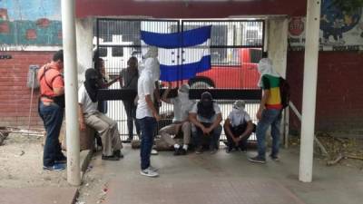 Los estudiantes cubren sus rostros afirmando que temen represalias y colocan una bandera en señal de protesta en el Intae de San Pedro Sula.