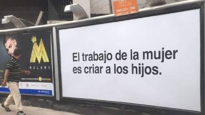 Un hombre camina de frente por un cartel misógino que es parte de una campaña publicitaria.