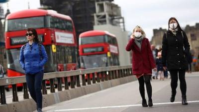 Transeúntes con mascarillas se protegen del coronavirus mientras caminan en Londres.