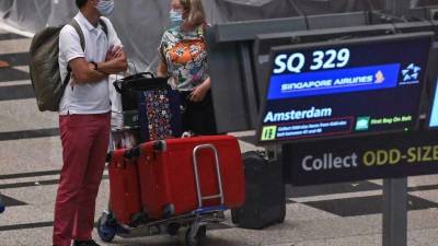 Dos pasajeros con mascarilla llegados de Ámsterdam recogen su equipaje en el aeropuerto Changi de Singapur.