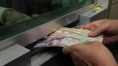Un cajero de una institución bancaria entrega billetes de diferentes denominaciones a un usuario.