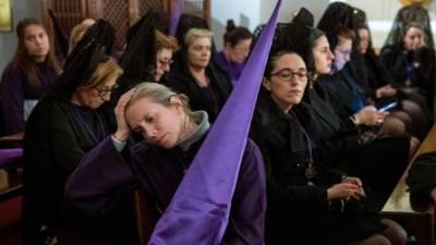 Mujeres con mantilla y nazarenos permanecen resguardados de la lluvia tras la suspensión de las procesiones que había programadas en el centro de la capital. Foto EFE