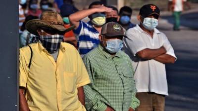 Las personas usan máscaras faciales contra la propagación del nuevo coronavirus mientras hacen cola en una calle de Tegucigalpa. Foto AFP