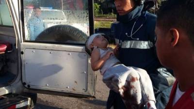 Un rescatista carga a una niña tras el accidente entre un camión y un vehículo turismo en Villanueva, Cortés.