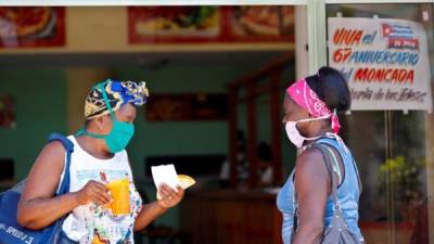 Dos mujeres protegidas con tapabocas conversan en la entrada de una cafetería.