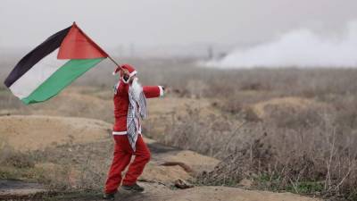 Un palestino disfrazado de Santa Claus ondea una bandera durante una manifestación contra la decisión del presidente de los Estados Unidos de reconocer Jerusalén como la capital de Israel, en el este de la Franja de Gaza. EFE