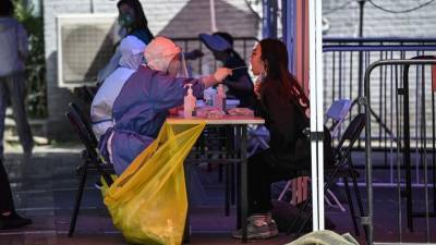 Un trabajador de la salud toma una muestra de hisopo de una mujer para realizarle la prueba del coronavirus en un sitio de prueba improvisado afuera de un museo en una calle de Beijing.