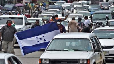 Los taxistas sostienen una bandera hondureña mientras bloquean un camino para protestar por la demanda de alimentos y ayuda económica en Tegucigalpa. Foto AFP