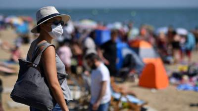 Una mujer que usa PPE una máscara facial como medida preventiva contra la propagación de COVID-19, llega a la playa en Inglaterra. Foto AFP