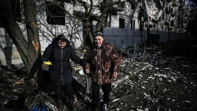Una pareja pasa junto al cuerpo de un familiar fuera de un edificio destruido después de los bombardeos en la ciudad de Chuguiv.