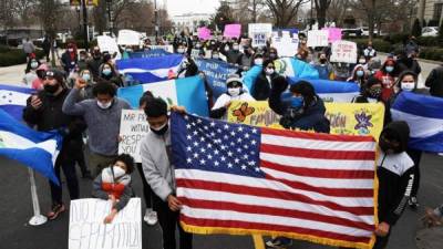Decenas de hondureños sostienen pancartas y banderas estadounidenses mientras marchan dirección a la Casa Blanca hoy, en Washington (EE.UU.).