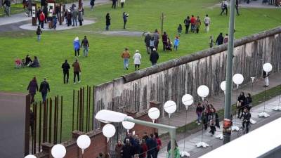 Ciudadanos pasean bajo los globos que reconstruyen el trazado del antiguo Muro, ante la Puerta de Brandenburgo.