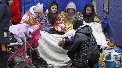 Refugiados ucranianos, cubiertos con mantas, se recuperan frente a una carpa después de pasar el cruce fronterizo rumano-ucraniano en Siret, en el norte de Rumania, el 27 de febrero de 2022.