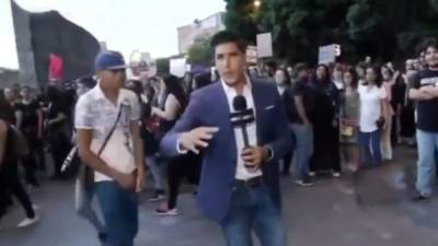 Momentos en que el periodista Juan Manuel Jiménez hacia su transmisión. El hombre de camiseta gris y gorra azul lo agredió.