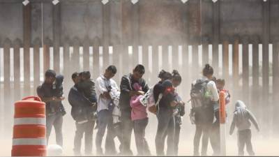 EL PASO, TX - MAY 17: Migrants shield themselves from blowing dust while being detained after crossing to the U.S. side of the U.S.-Mexico border barrier (background) on May 17, 2019 in El Paso, Texas. The location is an area where migrants frequently turn themselves and ask for asylum after crossing the border. Approximately 1,000 migrants per day are being released by authorities in the El Paso sector of the U.S.-Mexico border amidst a surge in asylum seekers arriving at the Southern border. Mario Tama/Getty Images/AFP
