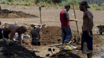 Gravediggers wearing suits and face masks to prevent the spread of the new coronavirus, COVID-19, bury a dead person at the 'Jardínes del Recuerdo' Cemetery, in Managua on May 15, 2020. - Nicaraguan residents and doctors fear that the country reaching a 'chaotic situation' due to the fast spread of COVID-19, without measures to contain the pandemic and aggravated by official secrecy over those affected. (Photo by INTI OCON / AFP)