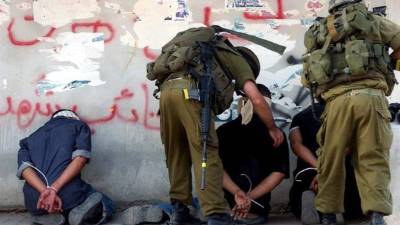 Unos soldados israelíes detienen y colocan contra la pared a unos palestinos que permanecen con las manos atadas y los ojos vendados en la ciudad de Salfit (Cisjordania). EFE/Archivo
