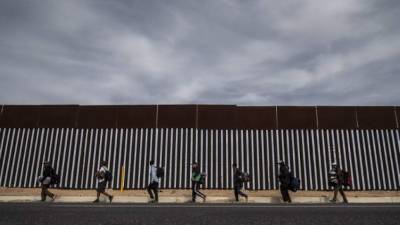Central American migrants -mostly Hondurans- moving in a caravan towards the United States in hopes of a better life, walk along the metal fence on the border between Mexicali in Mexico's Baja California State, and Calexico, in California, US, on November 19, 2018. - US President Trump has sent about 5,800 troops to the border to forestall the arrival of large groups of Central American migrants travelling through Mexico and towards the US, in a move critics decry as a costly political stunt to galvanize supporters ahead of midterm elections earlier this month. (Photo by Pedro PARDO / AFP)