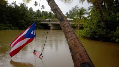 Fotografía de una bandera puertorriqueña y un columpio colgados de un árbol durante el paso del huracán Ernesto, en la desembocadura del río Hernández, este miércoles en Loiza, Puerto Rico.
