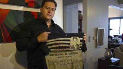 Sebastián Marroquín, hijo del fallecido capo de la droga colombiano Pablo Escobar, muestra una camiseta de su nueva línea de ropa Escobar Henao con la identificación de bachillerato de su parde en su casa en Buenos Aires, Argentina, el viernes 17 de agosto de 2012. Marroquín, quien se cambió legalmente el nombre y se mudó a Argentina en 1994 con su madre Maria Valeria Henao tras la muerte de su padre, dijo que creó la colección para enviar un mensaje de paz y reflexión sobre la historia de su familia. (Foto AP/Eduardo Di Baia)